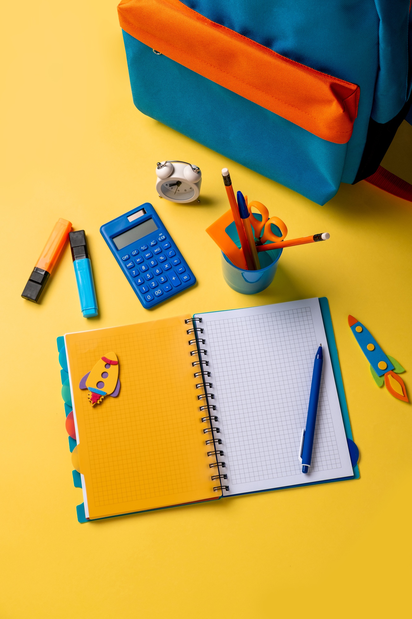 School backpack with colorful school supplies on yellow background.